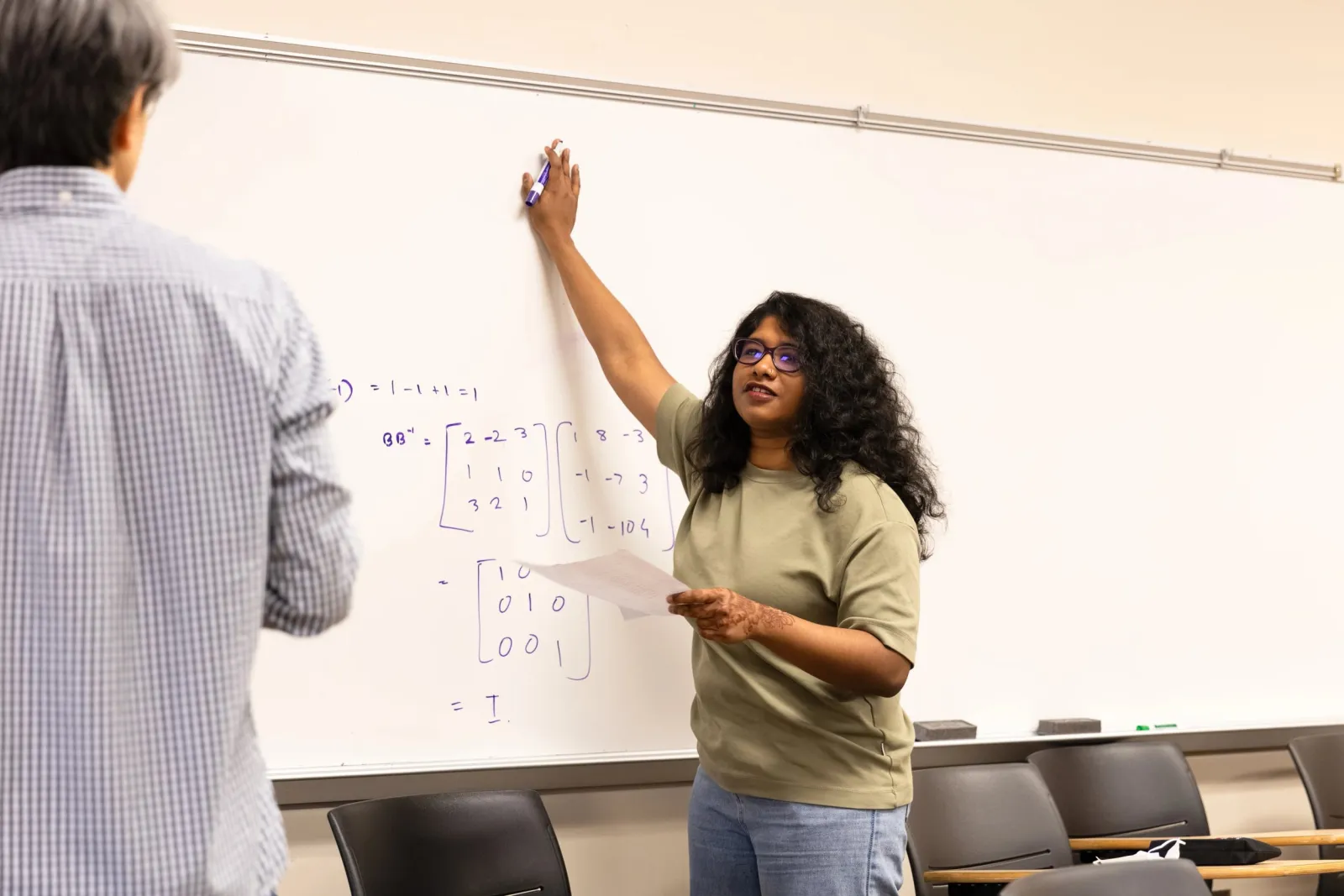 Physics student stands at whiteboard in classroom with prof