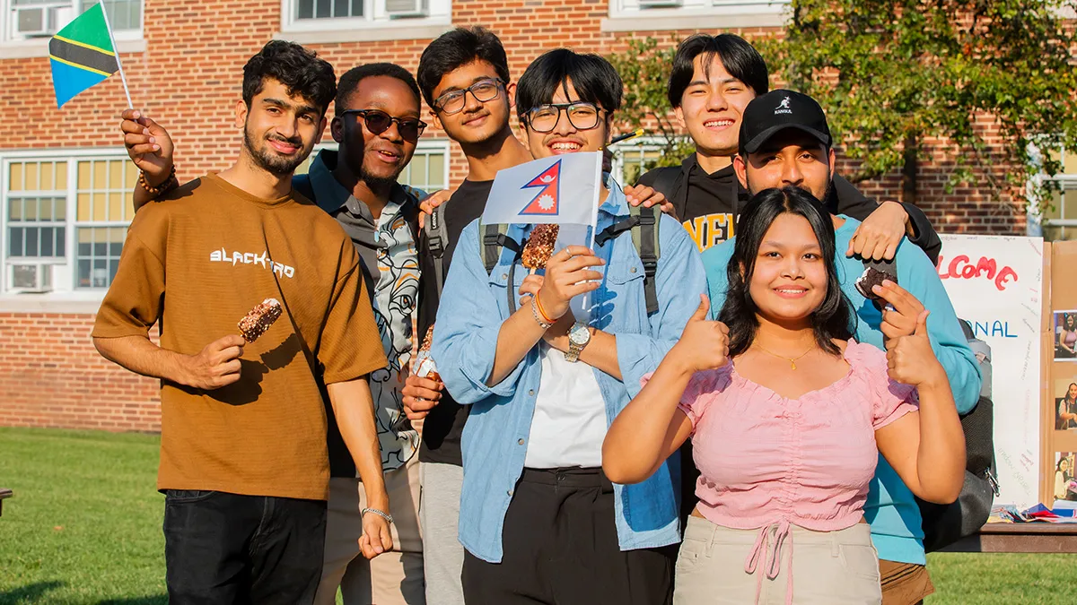 A photo of a group of students at a student activities fair, two of which are holding the flags of their home countries.