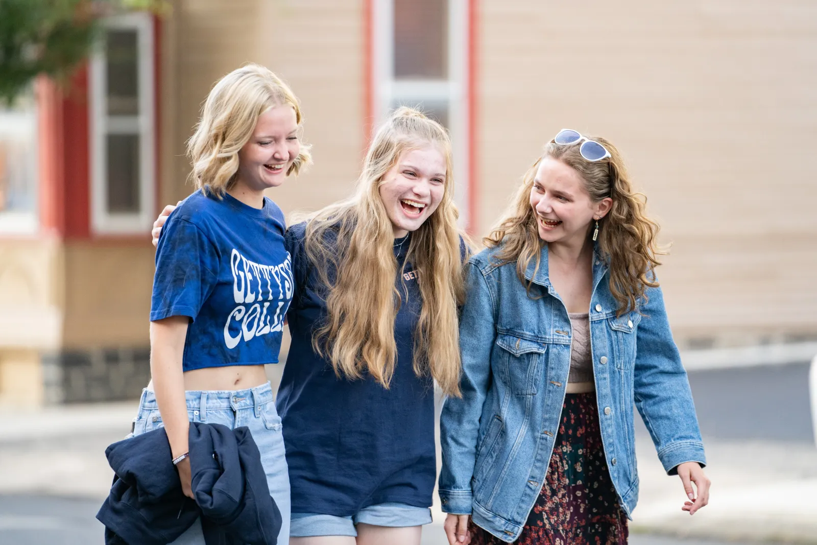 Three students walk together outdoors, smiling and laughing.
