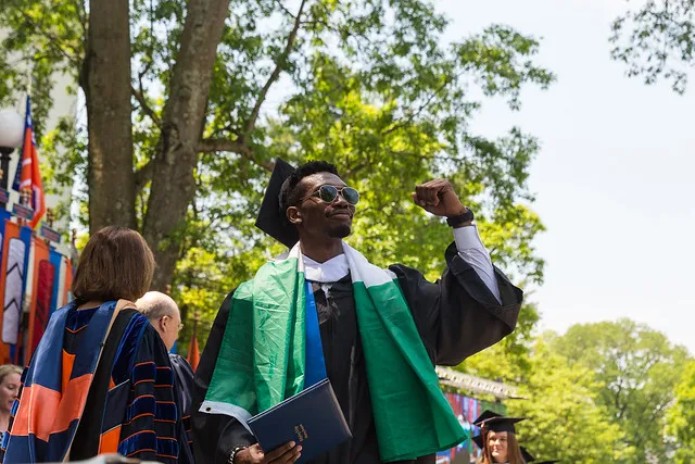Graduate celebrates outdoors with a raised fist and diploma.