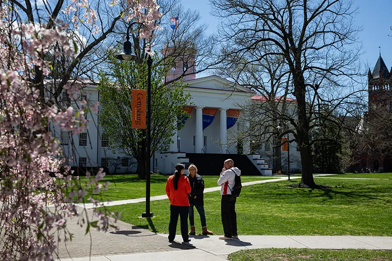 Three people stand on a campus sidewalk with Pennsylvania Hall in the background.