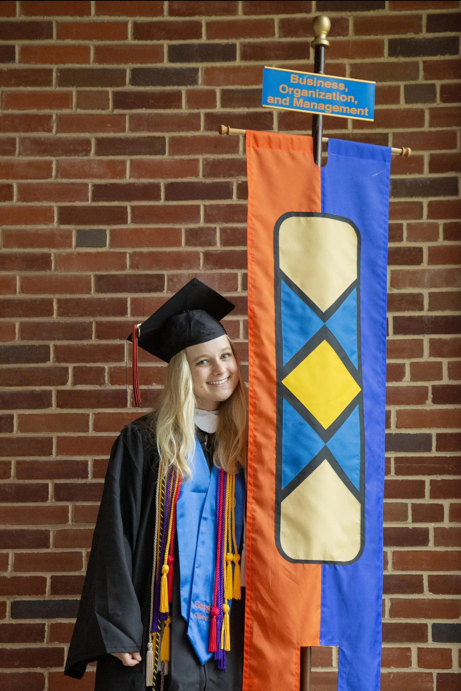 student in regalia carrying BOM Commencement banner