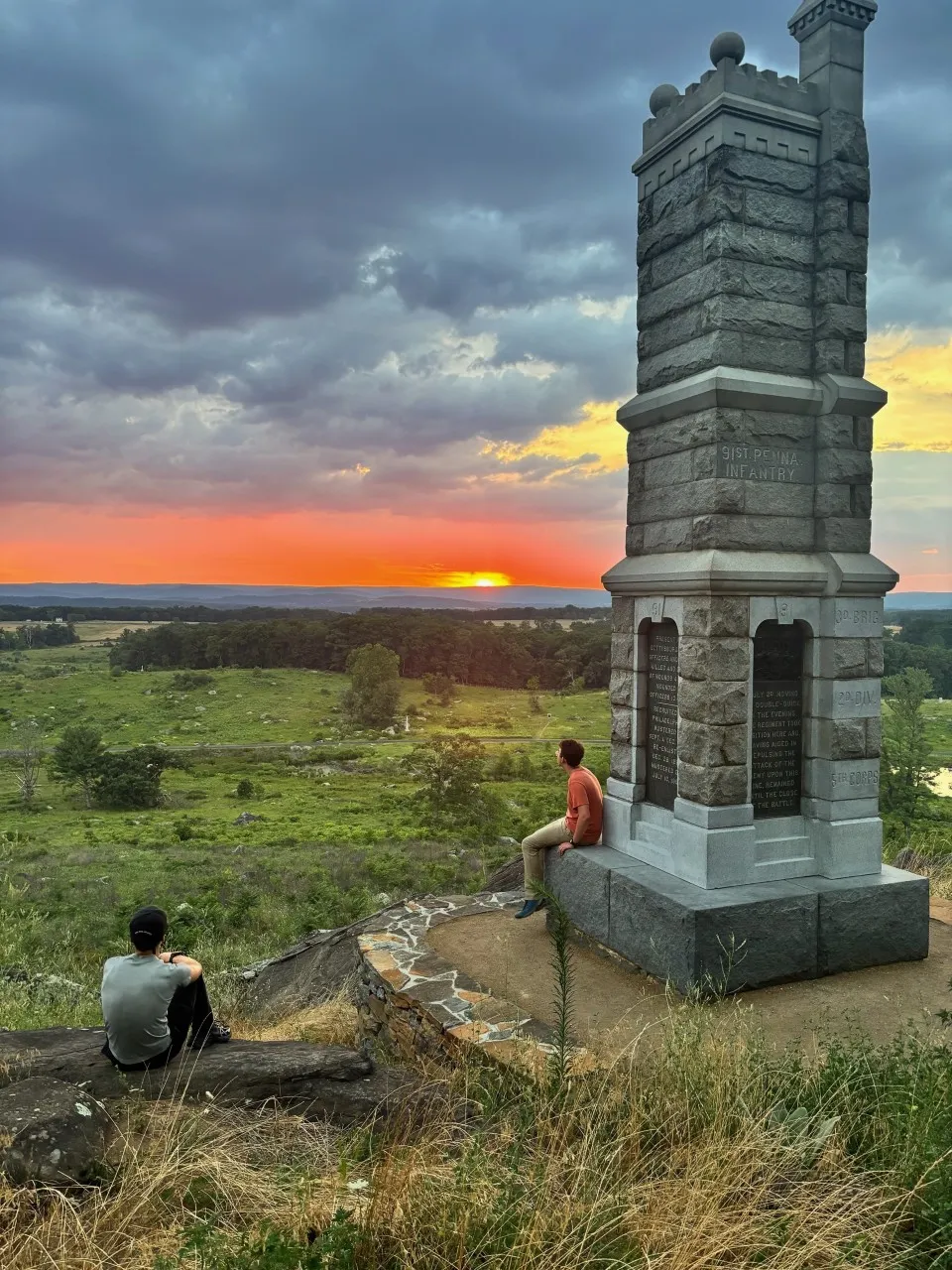 Students sit beside a Civil War monument overlooking the Gettysburg landscape at sunset.