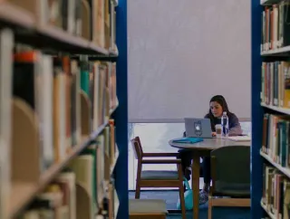 A woman works on her laptop while she sits in the library.