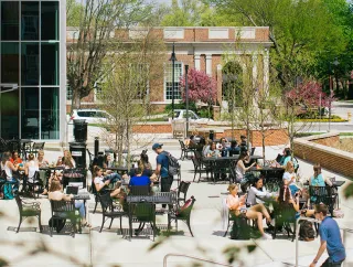 Students and tables on a sunny campus patio.