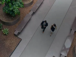 Two professionals walk along a landscaped path surrounded by trees and planters.