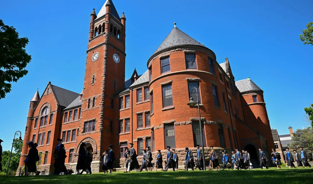 graduates process in front of large brick building