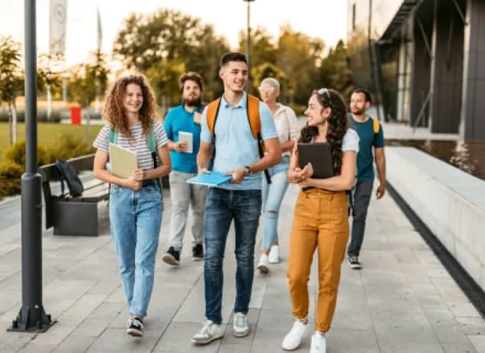 Group of students walking across campus together while talking and carrying books and backpacks.