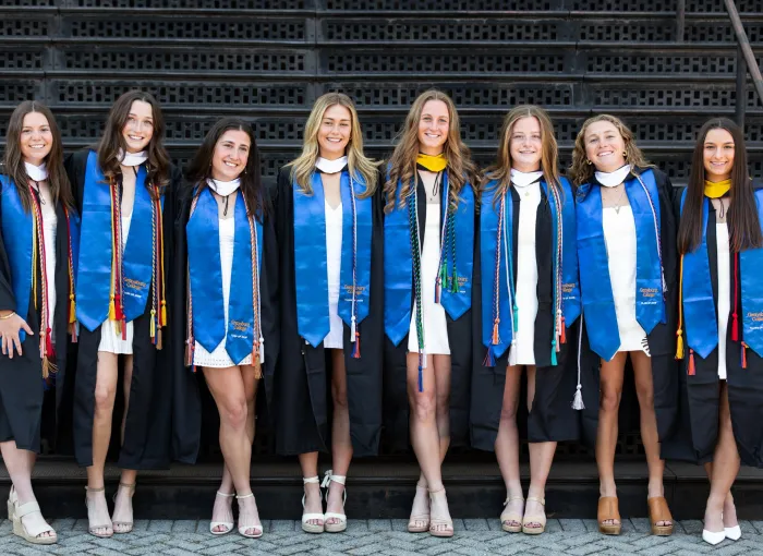 female grads in regalia pose together in front of steps