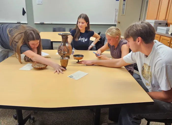 students examie ancient pottery at a table
