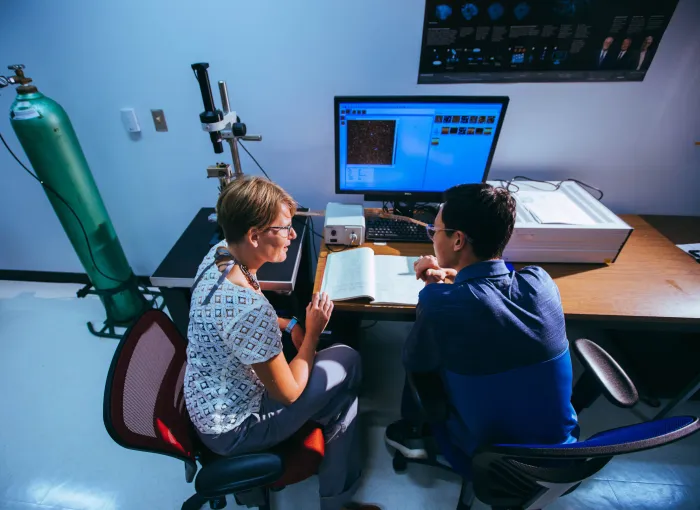 prof and student look at book together at desk in lab