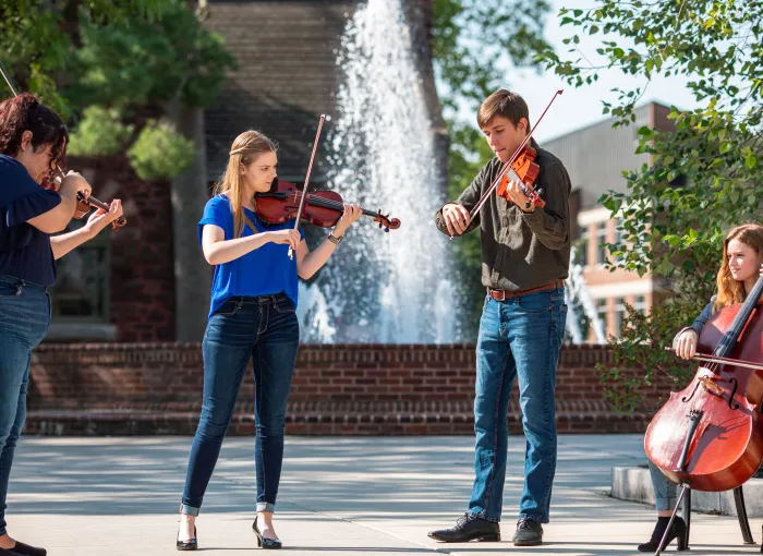 Music students play their instruments together in front of a fountain