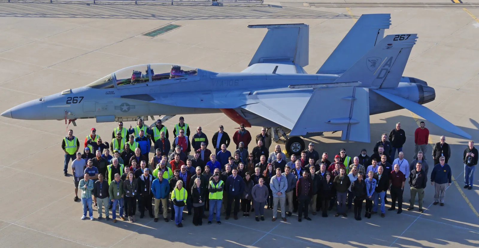 large group of people pose on ground in front of parked fighter jet
