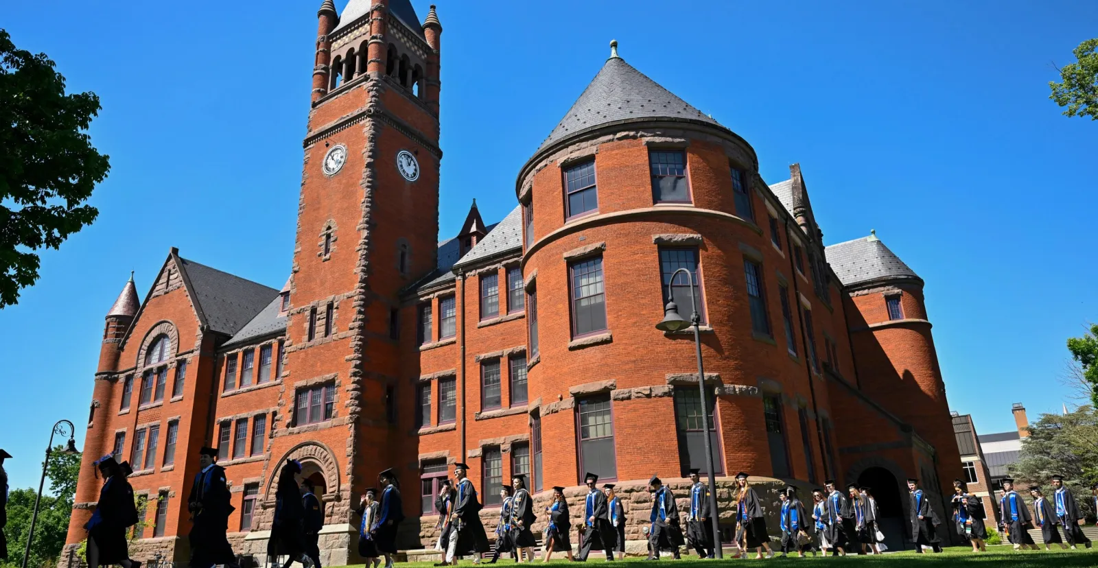 graduates process in front of large brick building