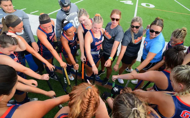 Field hockey team members putting their hands together in the middle of a circle