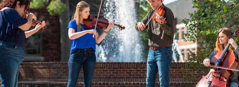Music students play their instruments together in front of a fountain