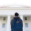 student with backpack faces white building with pillars