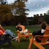 students sit in chairs outdoors in twilight under string lights